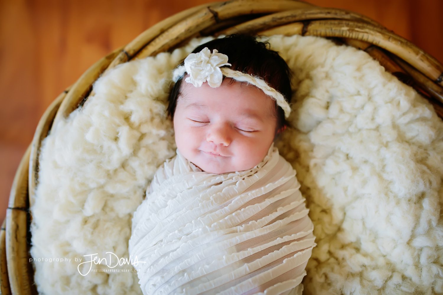 Baby swaddled with cream ruffled blanket in a basket with headband