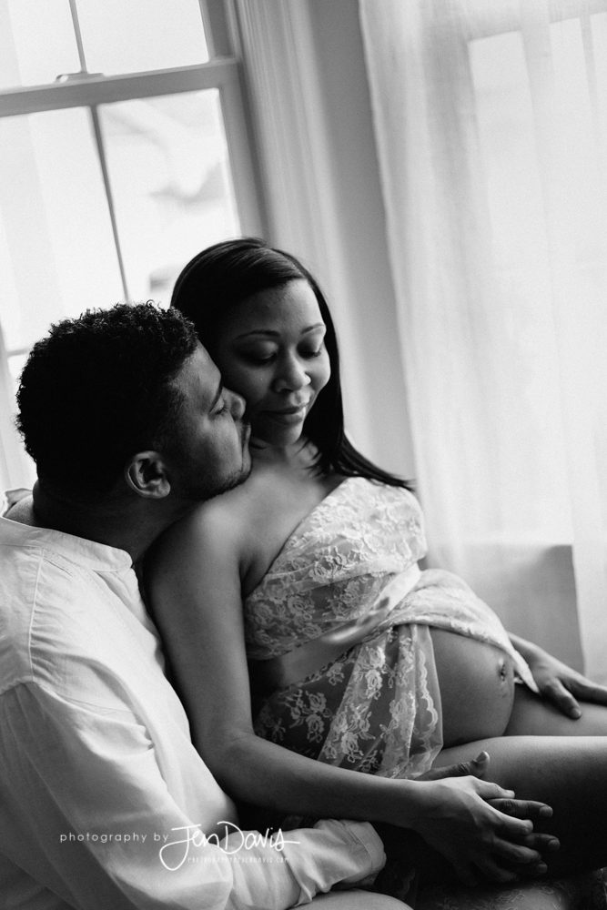 pregnant woman sitting with husband kissing her in black and white