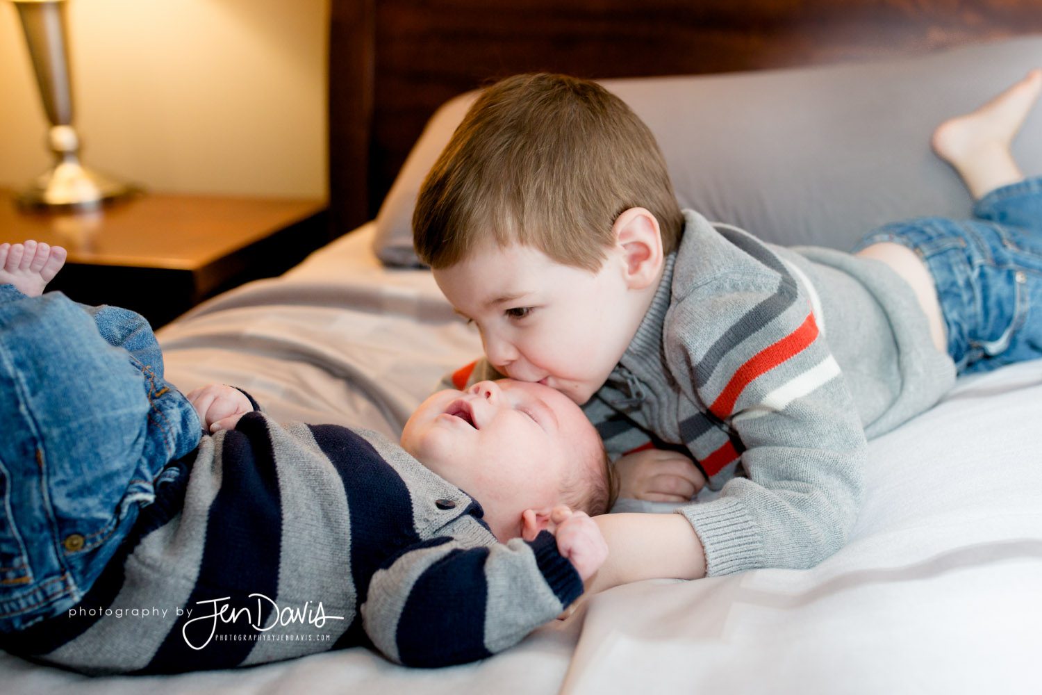 big brother kissing little baby on a bed