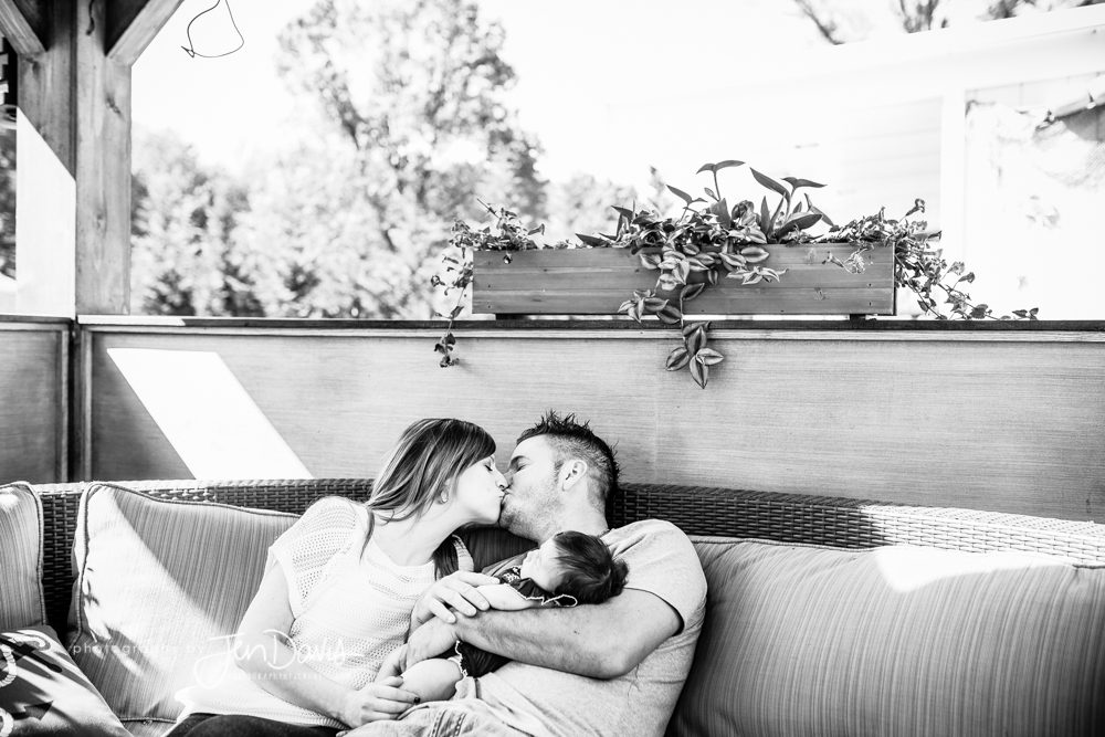 black and white of mom and dad kissing with baby