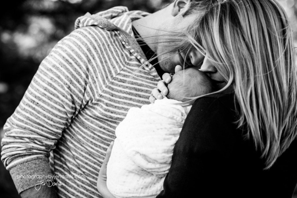 black and white of parents kissing a baby