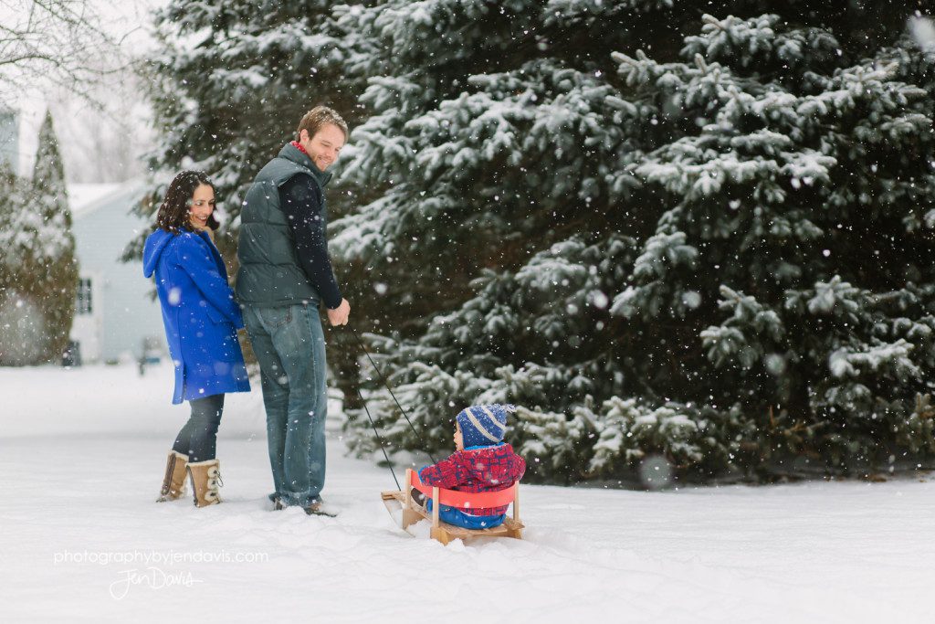 mom and dad pulling boy in sled in the snow