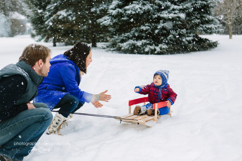 mom and dad pulling boy in sled in the snow