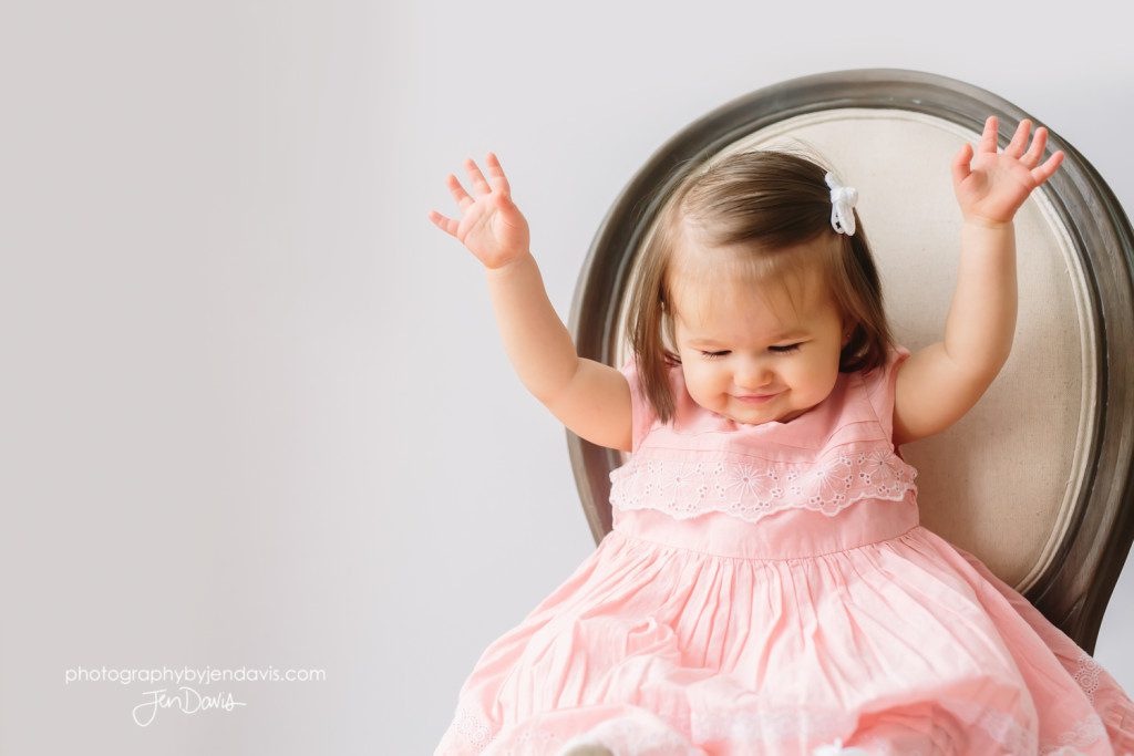 1 year old girl in pink dress sitting on chair