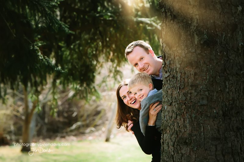 family of 3 peeking out from behind a tree
