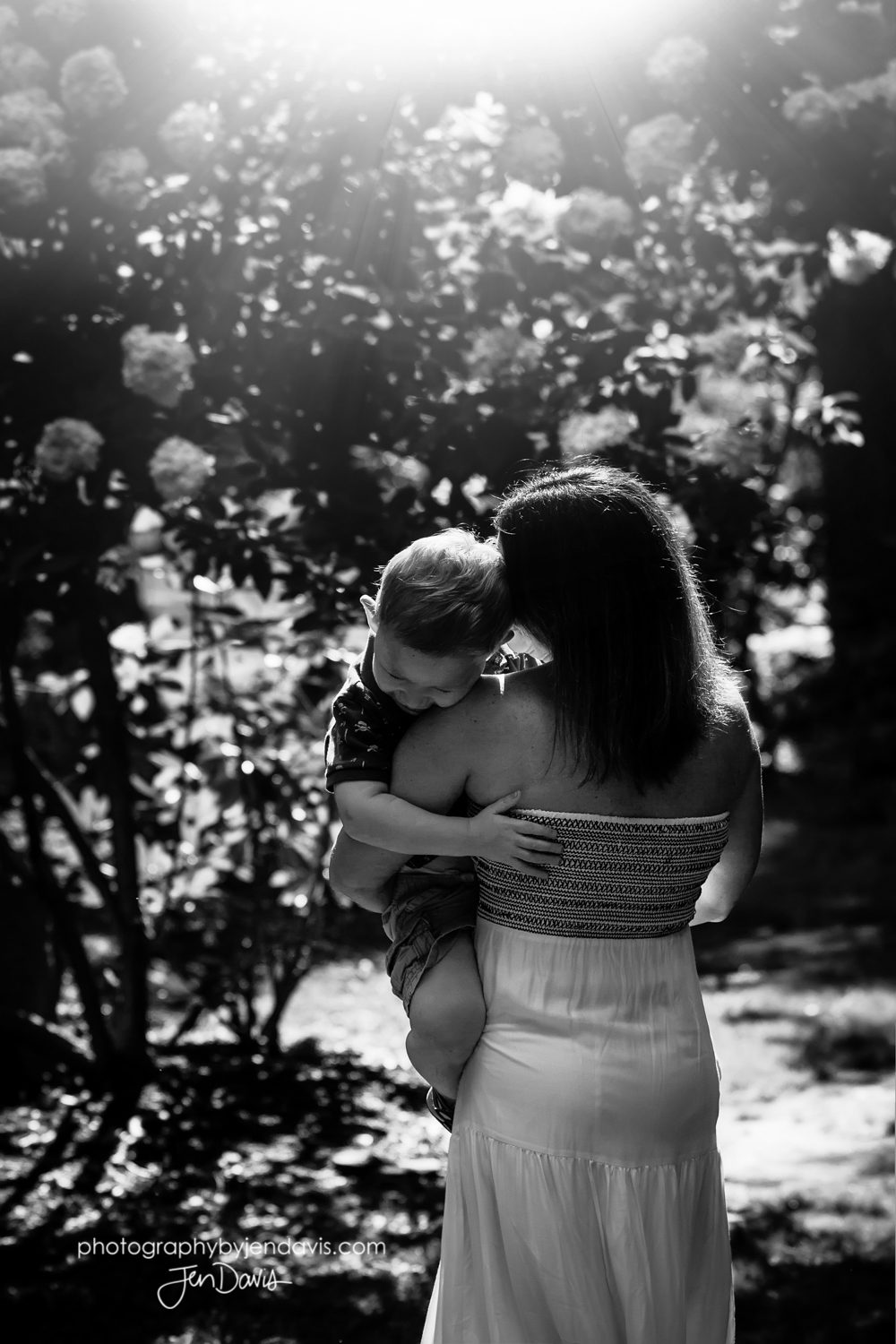 black and white image of mom hugging son in sunlight