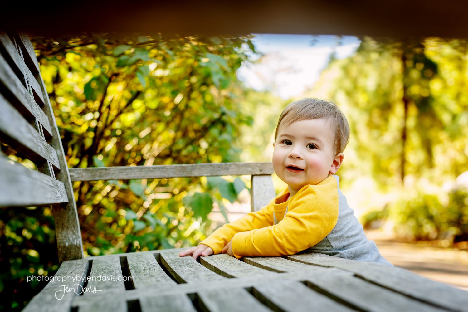 1 year old boy holding onto bench in the park